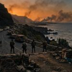 Retén militar en una carretera costera volcánica al atardecer, con autos abandonados y humo en el horizonte