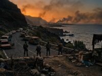 Retén militar en una carretera costera volcánica al atardecer, con autos abandonados y humo en el horizonte