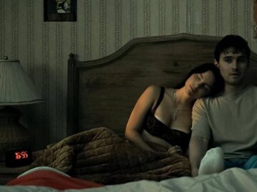 Una pareja en una habitación con papel tapiz antiguo y un reloj despertador, en una escena de terror romántico